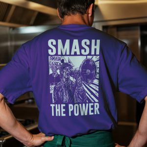 Uomo di spalle con t-shirt viola acceso e grande stampa chiara “SMASH THE POWER” con manifestanti e megafono